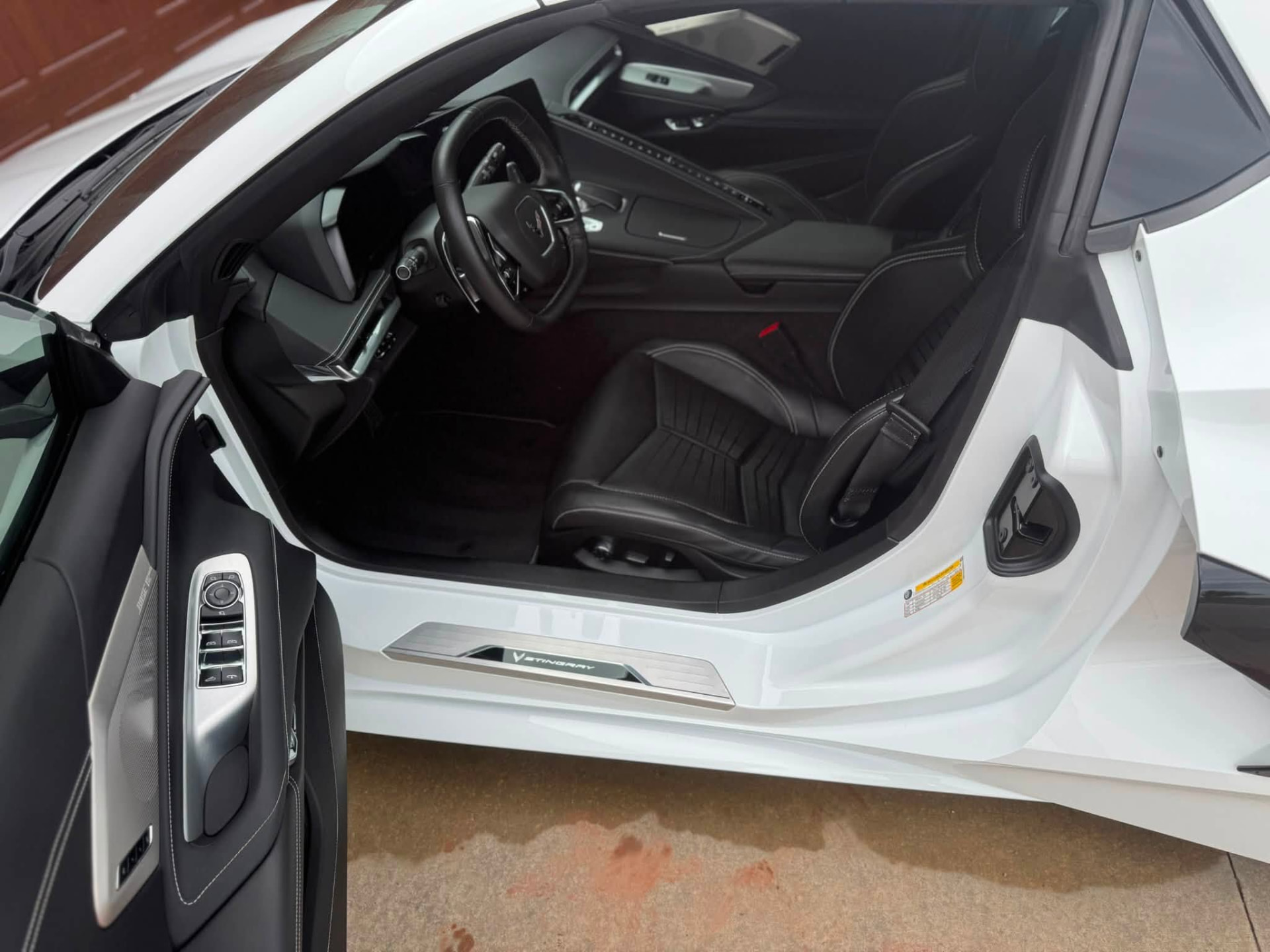 Driver door open on a white C8 Corvette showing a freshly detailed black leather interior and clean door sill