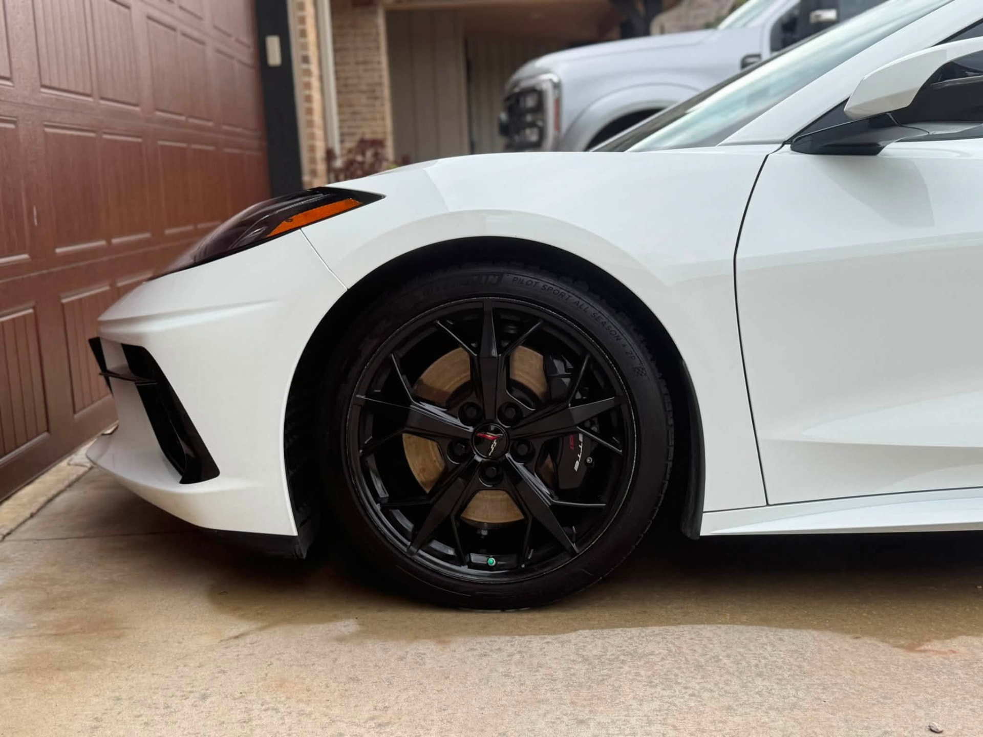 Front wheel and fender of a white C8 Corvette with clean black wheel and dressed tire after detailing